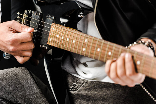 partial view of male rock musician in leather jacket playing on electric guitar isolated on white