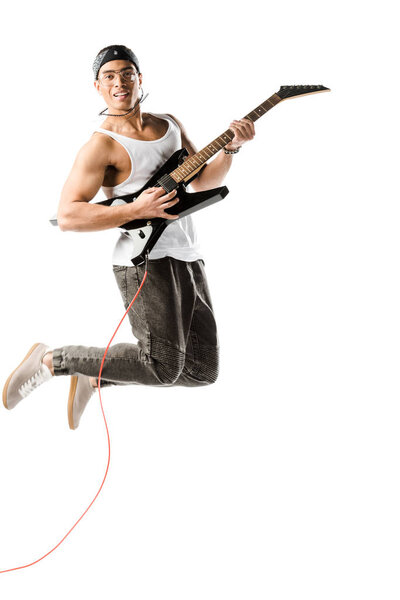 happy young male rocker jumping and playing on electric guitar isolated on white