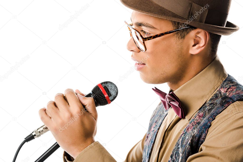 side view of handsome mixed race man in hat singing in microphone isolated on white