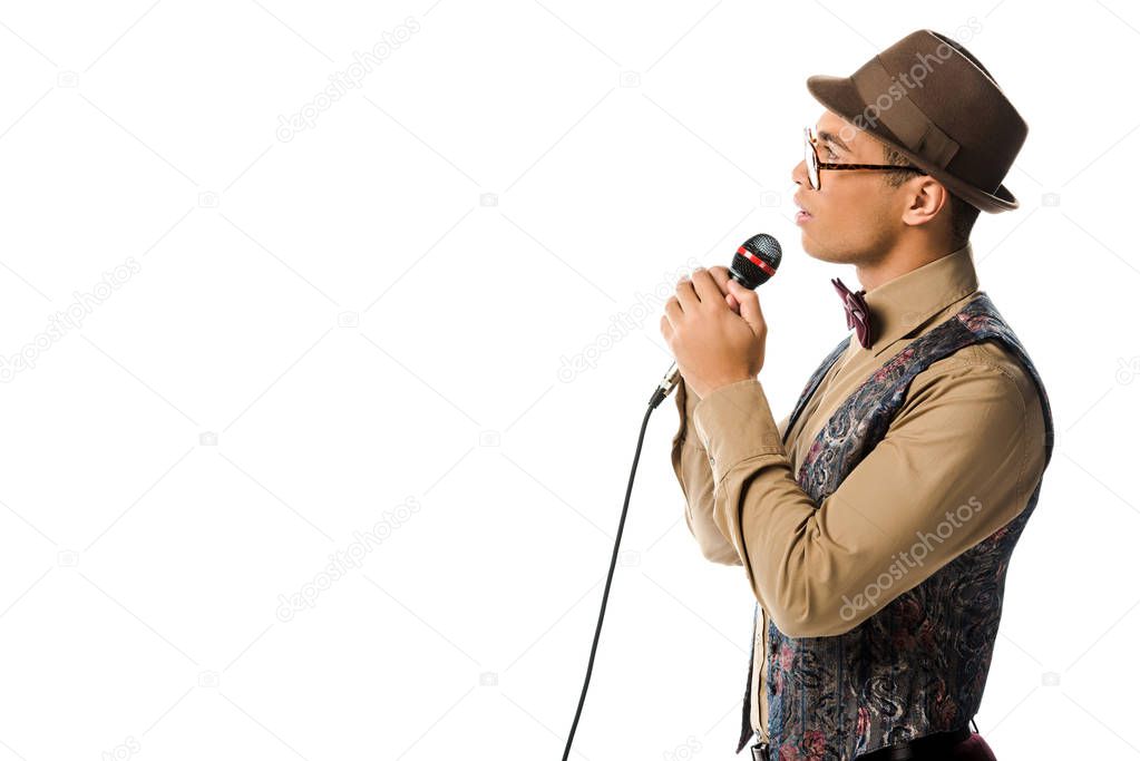 side view of mixed race male musician in hat singing in microphone isolated on white