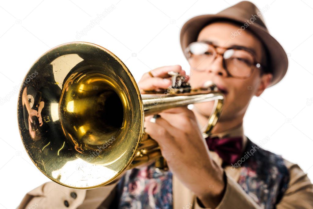 selective focus of mixed race male musician in stylish hat and eyeglasses playing on trumpet isolated on white 