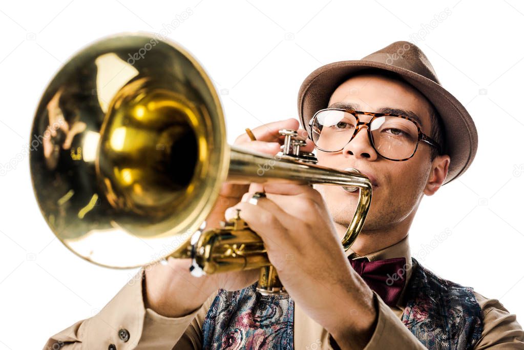 close up portrait of young mixed race man in stylish hat and eyeglasses playing on trumpet isolated on white 