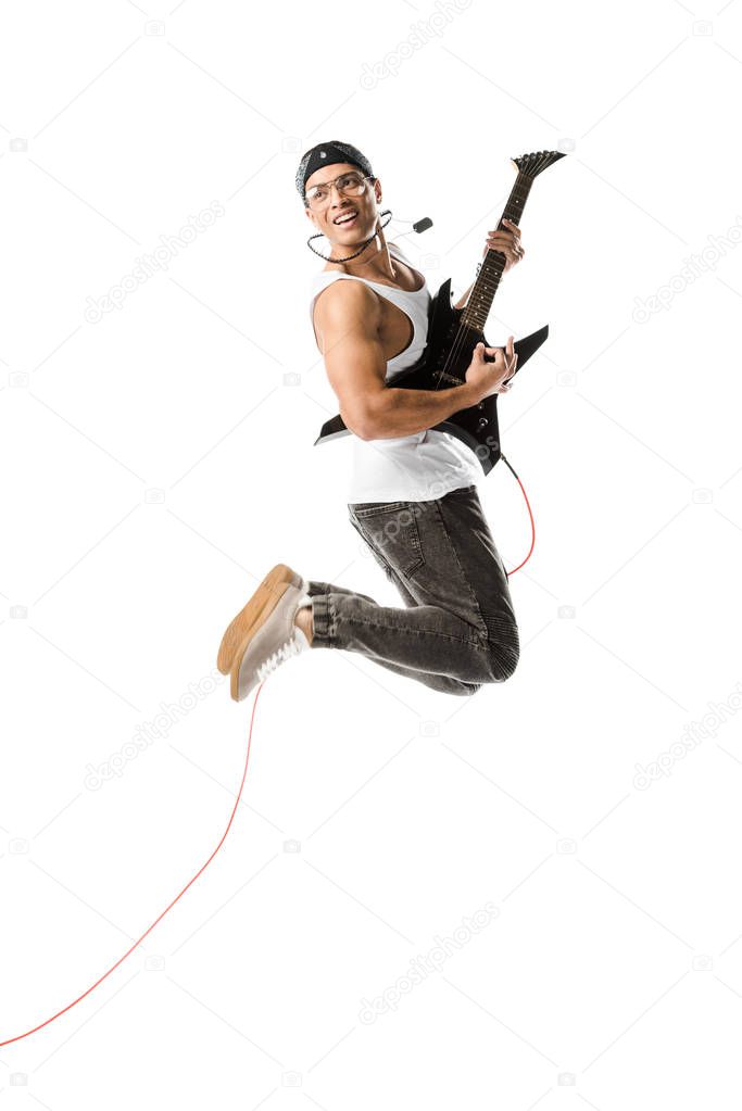 cheerful young man jumping and playing on electric guitar isolated on white