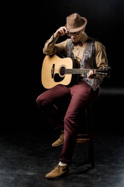 siyah sandalyede otururken akustik gitar ile poz şapkalı şık genç adam 