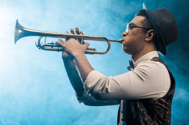 Trompet üzerinde dramatik aydınlatma ve duman ile sahnede oynarken jazzman yan görünüm