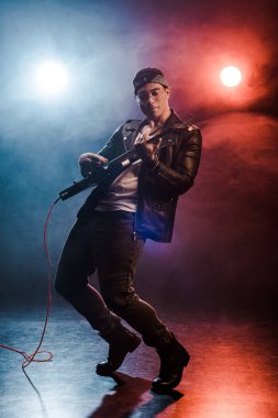 handsome stylish rocker in leather jacket performing on electric guitar on stage with smoke and dramatic lighting  clipart