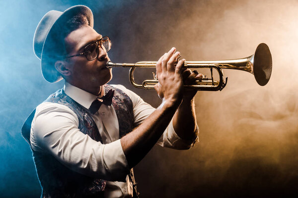 young jazzman playing on trumpet on stage with dramatic lighting and smoke