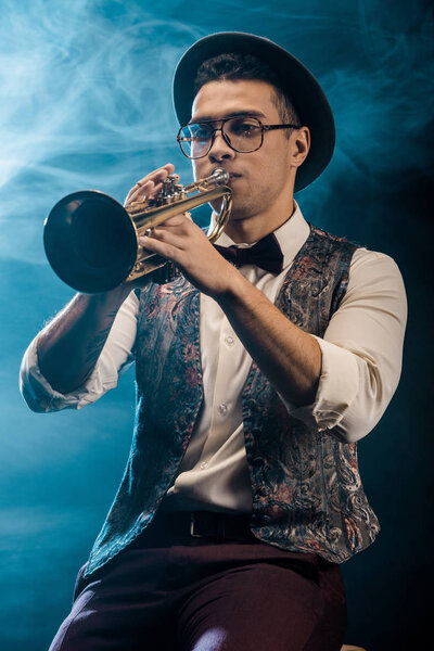 confident young jazzman playing on trumpet on stage with dramatic lighting and smoke