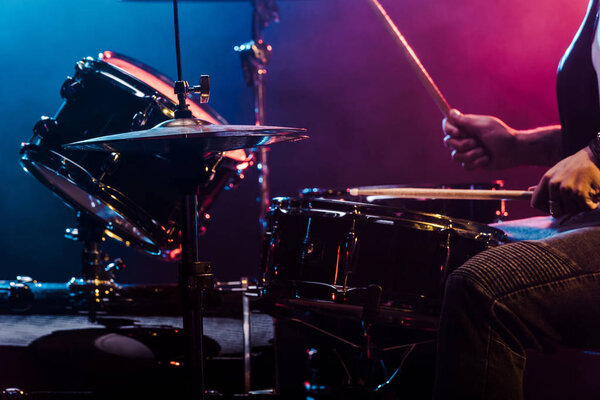 обрезанный кадр мужчины-музыканта, выступающего на барабанах во время рок-концерта на сцене
