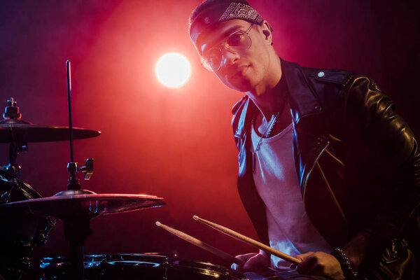 handsome male musician in leather jacket playing drums during rock concert on stage  
