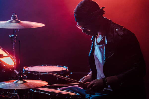 mixed race male musician in leather jacket playing drums during rock concert on stage  