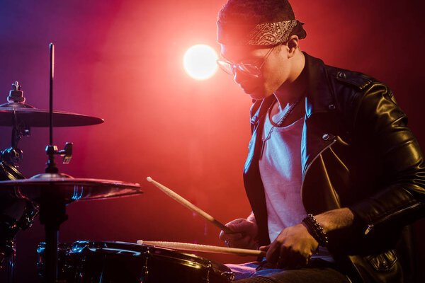 young male musician in leather jacket playing drums during rock concert on stage  