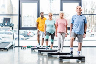 mutlu çok ırklı üst düzey sporcular spor salonuna adım platformları yakınındaki ayakta