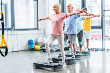 multicultural senior athletes synchronous exercising on step platforms at sports hall clipart
