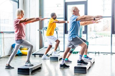 çok kültürlü üst düzey sporcular spor salonunda adım platformlarda zaman uyumlu egzersiz yan görünüm