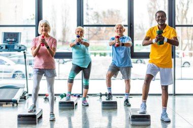 mutlu üst düzey çok kültürlü sporcu spor salonunda adım platformlarda dumbbells ile egzersiz zaman uyumlu