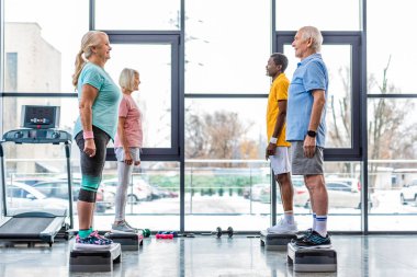çok kültürlü üst düzey sporcu ayakta spor salonunda yan yana adım platformlarda yan görünüm