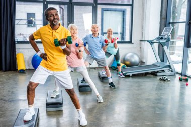 çok kültürlü üst düzey sporcu spor salonunda adım platformlarda dumbbells ile egzersiz zaman uyumlu