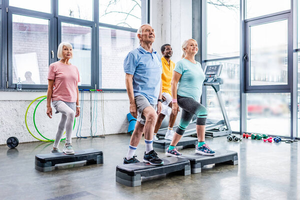 senior multicultural athletes synchronous exercising on step platforms at gym