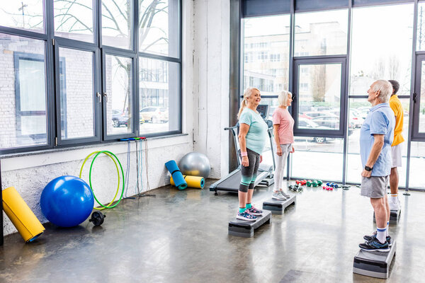 senior sportspeople standing on step platforms next to each other at gym