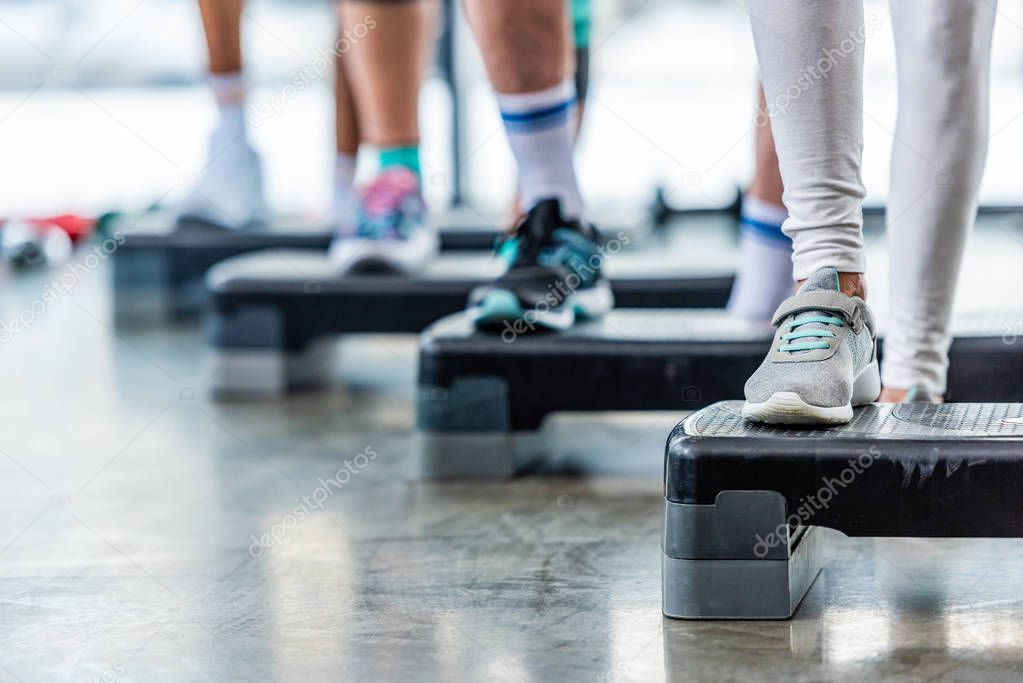 cropped shot of sportspeople doing exercise on step platforms at gym