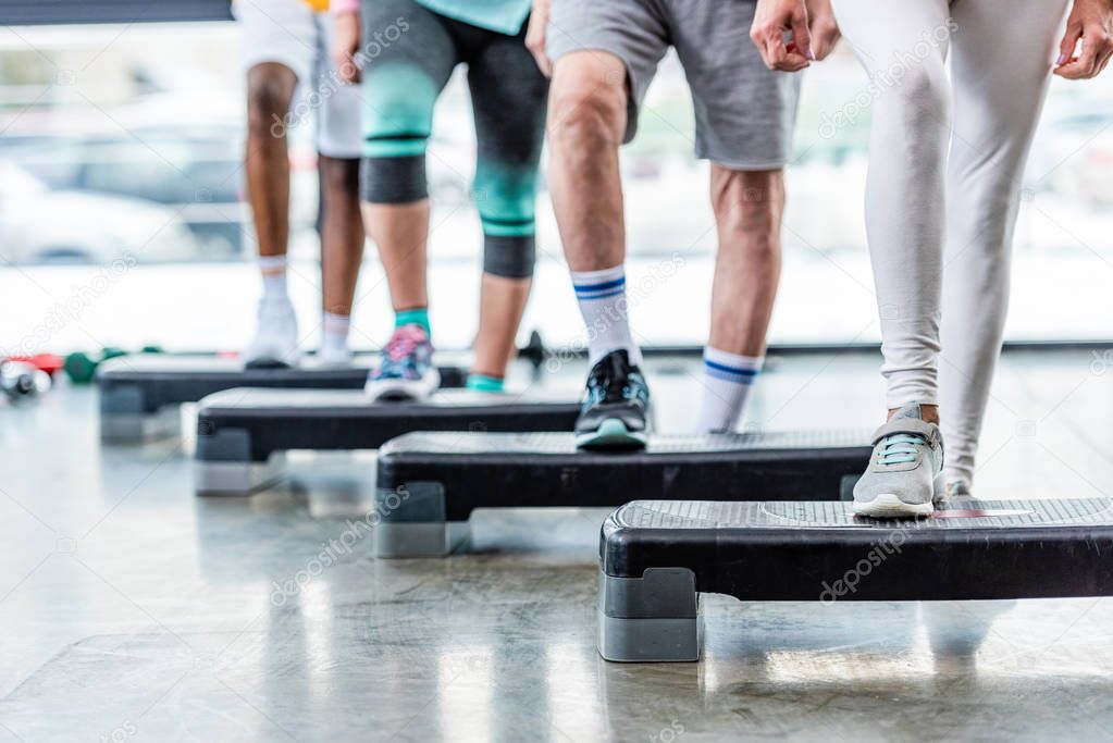 cropped image of sportspeople doing exercise on step platforms at gym