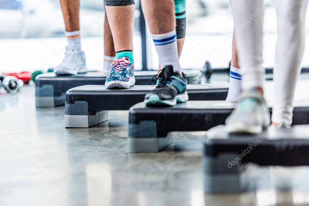 partial view of sportspeople doing exercise on step platforms at gym