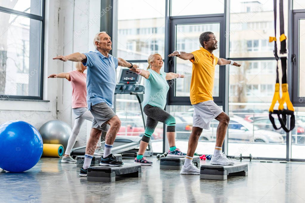 multicultural senior sportspeople synchronous exercising on step platforms at gym