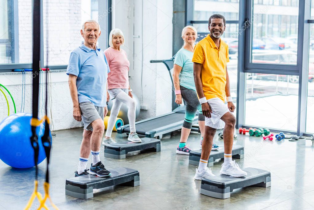 multiethnic senior athletes synchronous exercising on step platforms at gym