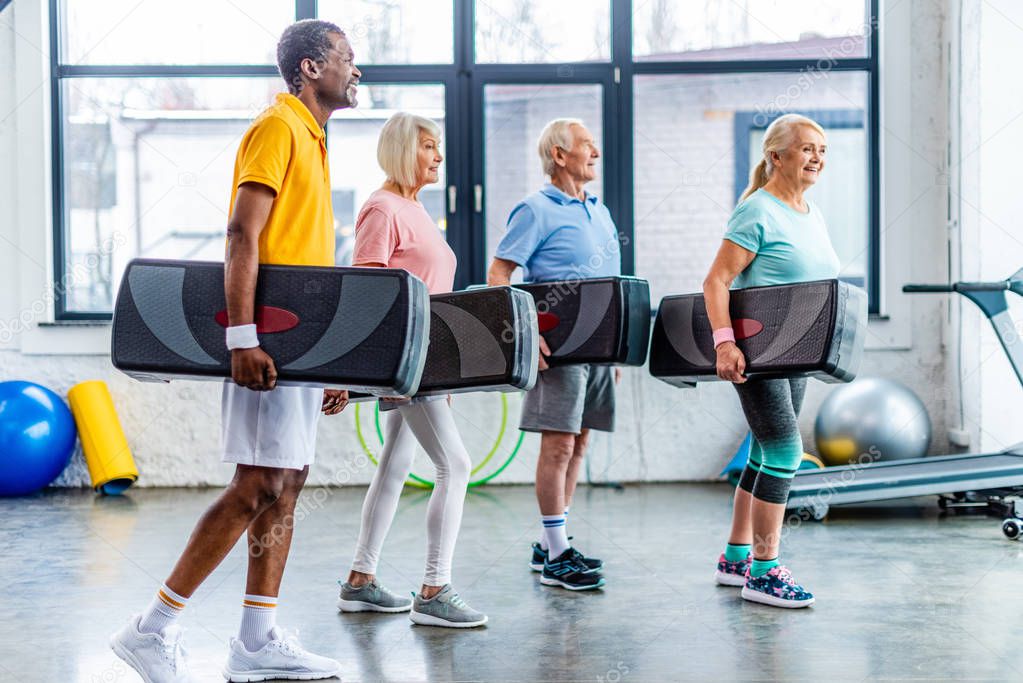 happy multiethnic sportspeople holding step platforms at gym