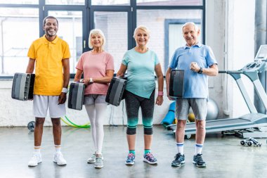 gülümseyen çok ırklı üst düzey sporcu spor salonunda adım platformlar holding