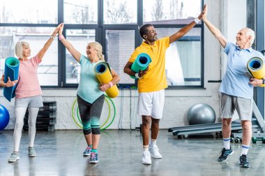 üst düzey çok ırklı sporcular spor salonunda birbirlerine yüksek beşli alarak fitness paspaslar ile gülüyor