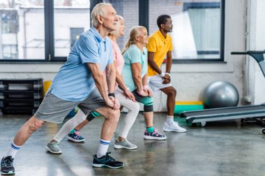 side view of senior multiethnic athletes synchronous stretching at gym clipart