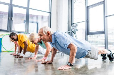 cheerful multiethnic senior sportspeople synchronous doing plank at gym clipart