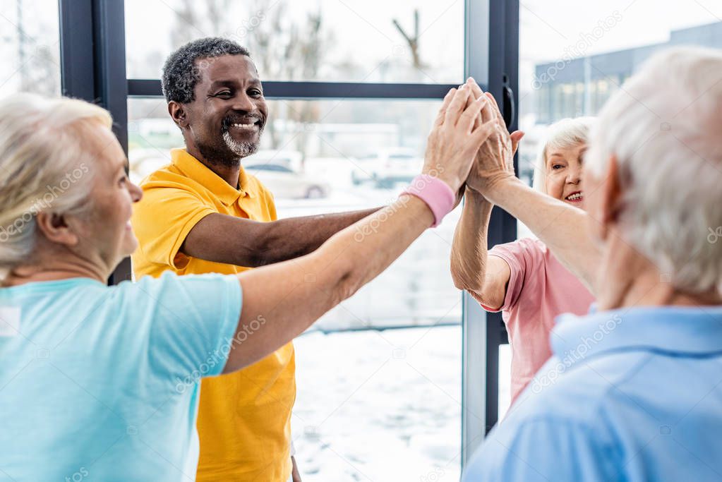 selective focus of senior multicultural sportspeople putting hands together at gym