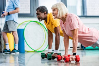tahta spor salonunda dumbbells ile yapıyor Interracial Olgun çift yan görünüm