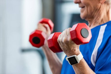 üst düzey sporcu spor salonunda dumbbells ile egzersiz yaparak smartwatch ile kısmi görünümünü