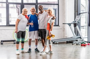 Kameraya bakıyor ve birbirimize spor salonunda kucaklayan neşeli çok kültürlü üst düzey sporcu 