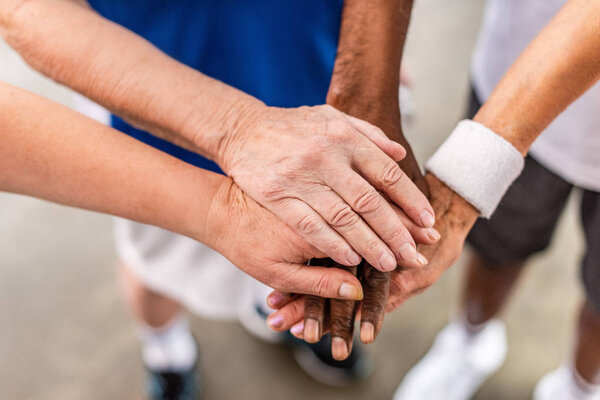 partial view of senior multiculutral sportspeople putting hands together at sports hall 