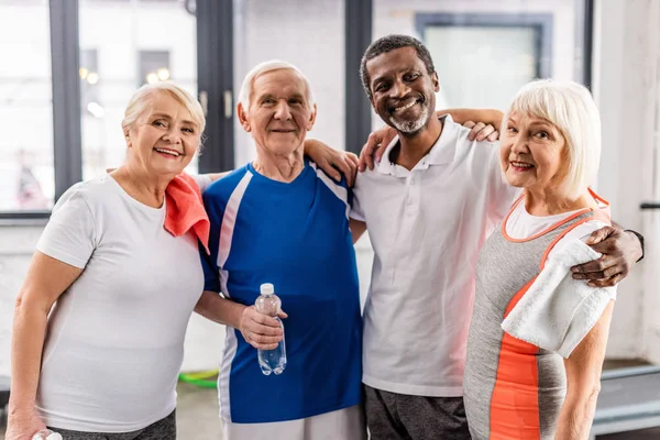 Alegre Multicultural Deportistas Senior Mirando Cámara Abrazándose Gimnasio —  Fotos de Stock