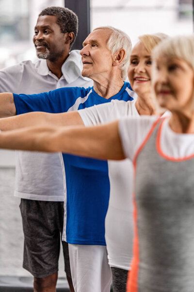 smiling senior multiethnic sportspeople synchronous exercising at sports hall