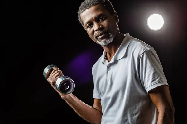 スポット ライトと黒地のダンベルの運動中央高齢者アフリカ系アメリカ人のスポーツマン — ストック写真