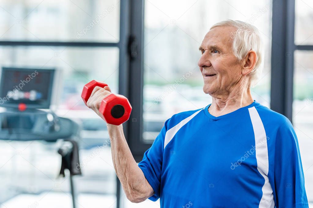 happy senior sportsman exercising with dumbbell at gym