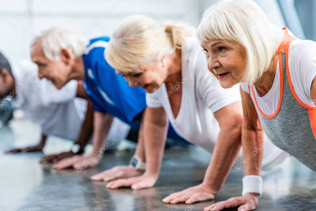 selective focus of senior sportswoman and her friends doing plank at gym