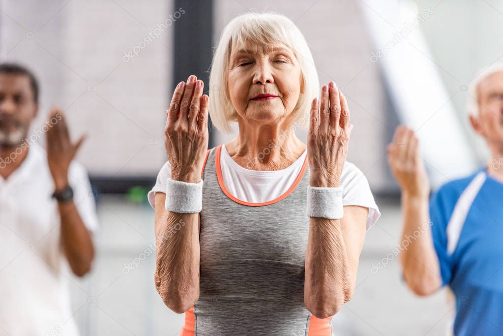selective focus of senior sportswoman with closed eyes making exercise at gym