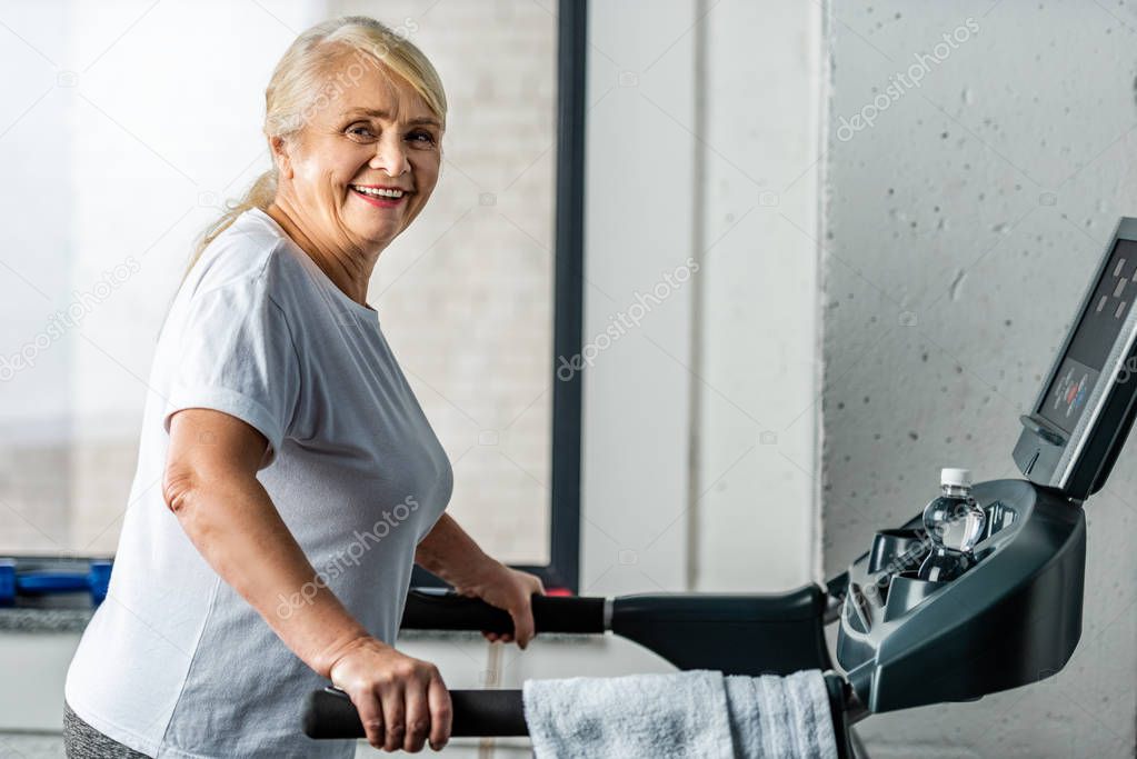 happy senior sportswoman running on treadmill at sports hall