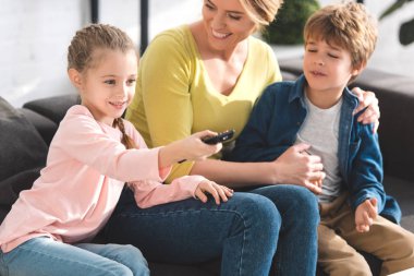 mutlu anne bakarak uzaktan kumanda kullanarak ve evde tv izlerken çocuklar