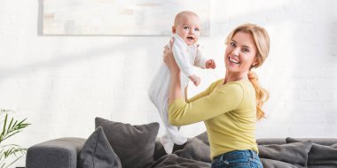 güzel bebek çocuk tutarak ve kameraya gülümseyen mutlu anne 
