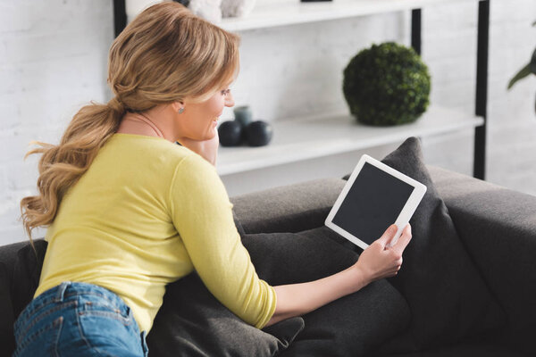 smiling woman sitting on couch and using digital tablet with blank screen 
