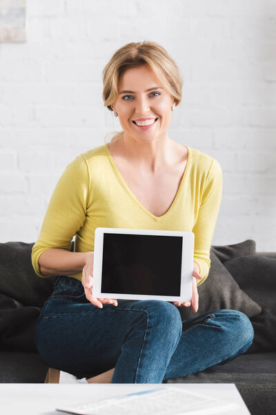 attractive woman holding digital tablet with blank screen and smiling at camera 